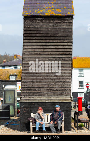 Zwei Männer sitzen auf einer Bank an einem sonnigen Tag vor der berühmten Hastings fisch Hütten, Hastings, East Sussex, Großbritannien Stockfoto