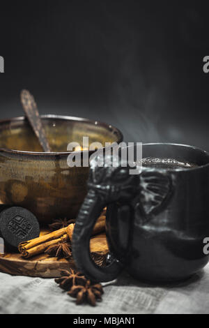 Kambodschanischen Teetasse mit Keramik Schüssel auf Holz Schneidebrett mit Zimt und Anis Samen über dunklen Hintergrund serviert. Stockfoto