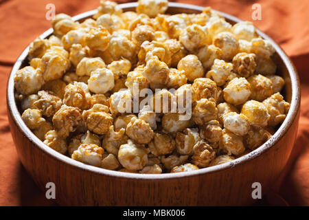 Hölzerne Schüssel mit süßem Popcorn auf orange Bettwäsche. Snacks und Essen für einen Film. Stockfoto