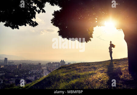 Frau in Silhouette mit Hut steigende Hand im Sunset City View Hintergrund. Das Leben in der Stadt. Stockfoto