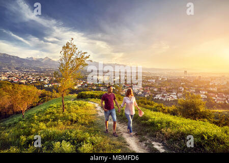 Yong Paar in rosa Kleidung Wandern im Park am Sonnenuntergang Blick auf die Stadt. Stockfoto