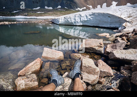 Die Beine des Menschen in Tracking Schuhe und Blick auf die schneebedeckten Gletscher auf dem See in die Berge Stockfoto