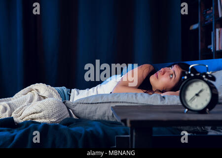 Bild von unzufriedenen Frau mit Schlaflosigkeit liegend auf Bett neben Wecker in der Nacht Stockfoto