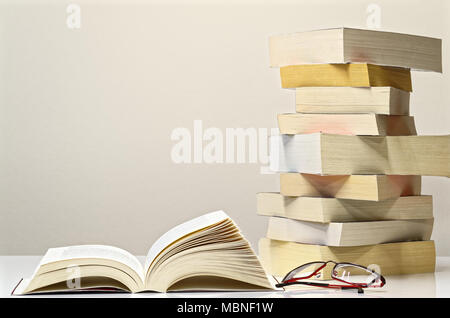 Buch, Brille und Stapel Bücher auf dem weißen Tisch Öffnen mit hellgrauem Hintergrund Stockfoto