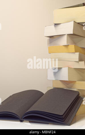 Schwarz Buch öffnen im Vordergrund der Stapel Bücher auf dem weißen Tisch und hellgrauen Hintergrund Stockfoto