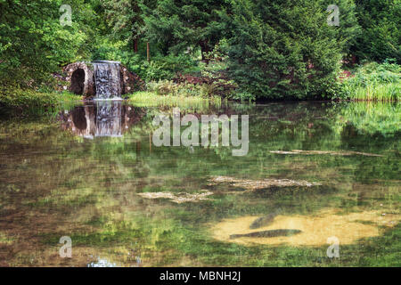 Rozendaal, Niederlande, 23. August 2014: Shells Grotte mit Wasserfall im Park von Schloss Rosendael während zwei grosse Karpfen Rest auf der Unterseite des Pon Stockfoto