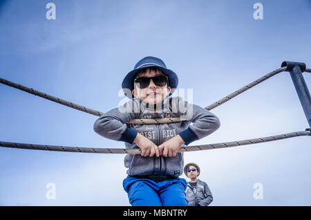 Ein Junge lehnt sich an einem Seil Zaun, wie er lächelt und posiert für ein Portrait. Stockfoto