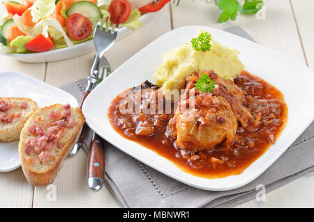 Kohlblätter gefüllt mit Hackfleisch, Sauce mit Speck und Zwiebeln, purree und Salat Stockfoto