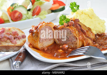 Kohlblätter gefüllt mit Hackfleisch, Sauce mit Speck und Zwiebeln, purree und Salat Stockfoto