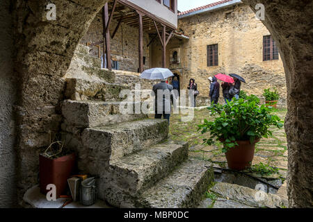 Feneos, Peloponnes/Griechenland. Besucher halten Regenschirme im Hinterhof in das Kloster St. George an einem regnerischen Tag Stockfoto