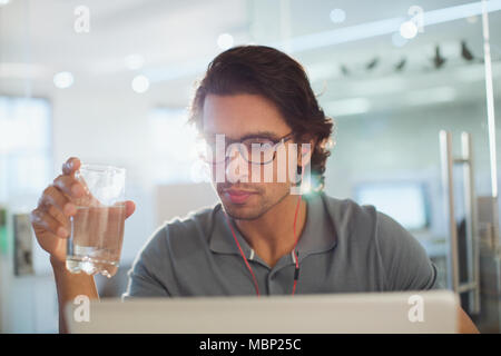 Geschäftsmann mit Kopfhörern Trinkwasser an Laptop gerichtet Stockfoto