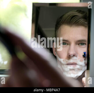 Reflexion von stattlicher Mann mit grünen Augen Rasur mit blauen Razor in kleinen Spiegel Stockfoto