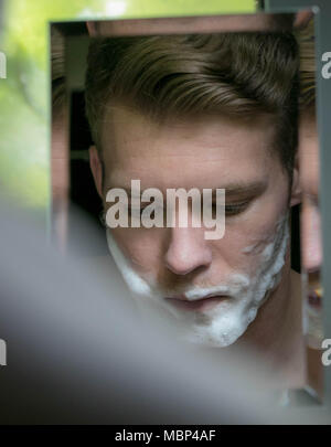 Reflexion von stattlicher Mann mit grünen Augen Rasur mit blauen Razor in kleinen Spiegel Stockfoto