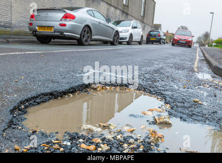 Schlagloch auf einer Asphaltstraße mit Regenwasser in England, Großbritannien. Beschädigte Fahrbahn. Straße, die sich in Not oder reparieren. Große Schlaglöcher. Sie auf das riesige Schlagloch. Stockfoto