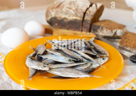 Ein kleiner Fisch Sardelle in einem orange Platte vor dem Hintergrund der Eier und Brot Stockfoto