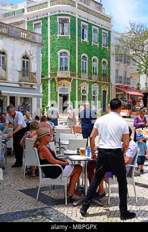 Touristen entspannen im Straßencafés in der Praça Luis de Camões mit einem grünen Fliesen- Traditionelle portugiesische Gebäude an der Rückseite, Lagos, Algarve, Portug Stockfoto