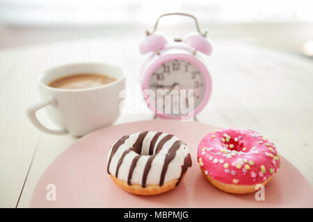 Leckere Donuts und Kaffee bereit für Frühstück, retro Wecker am Morgen zu Hause Stockfoto