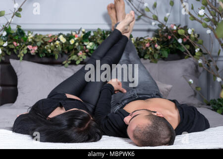 Wunderbare paar muslimischen Mann und seine schwangere Frau tragen schwarze Kleidung, einander an, während auf der grauen gemütliches Bett im Schlafzimmer liegen Stockfoto