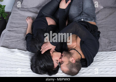 Hohe Betrachtungswinkel von wunderbaren Paar muslimischen Mann und seine schwangere Frau tragen schwarze Kleidung, Küssen, während auf der grauen gemütliches Bett im Schlafzimmer liegen Stockfoto