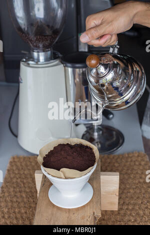 Hand Filterkaffee, Barista gießt Wasser auf Kaffee boden mit Filter, Kaffeemühle und eine Espressomaschine Hintergrund Stockfoto