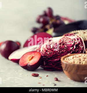 Zutaten zum Kochen, Kopieren, Ansicht von oben, flach. Lila Gemüse, Obst auf grauem Hintergrund. Violett Aubergine, Rüben, Blumenkohl, lila Bohnen, Zwetschgen, Zwiebel, Traube, Quinoa, Reis. Stockfoto