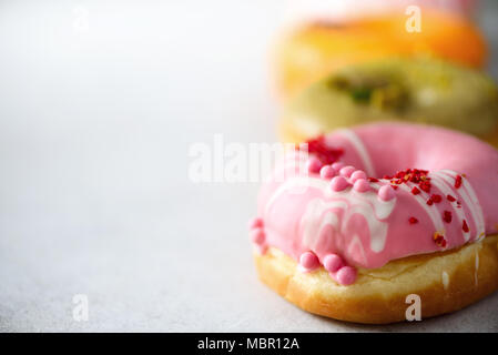 Stapel von Verglasten bunt sortierte Donuts mit Streuseln auf grauem Zement Hintergrund. Kopieren Sie Platz. Süße Krapfen für Kinder Stockfoto