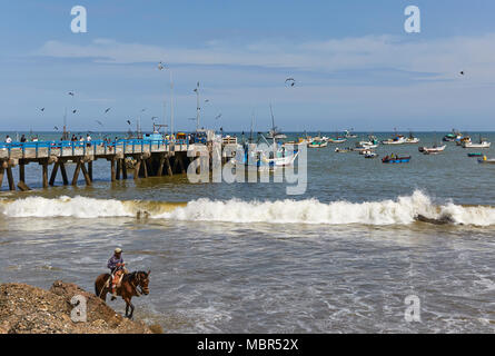 Fischer auf Mancora Fishing Pier, ihre Boote entladen und die Überwachung der Verteilung Ihrer Fische, während ein Pferd Reiter Ausritte am Strand entlang in die F Stockfoto