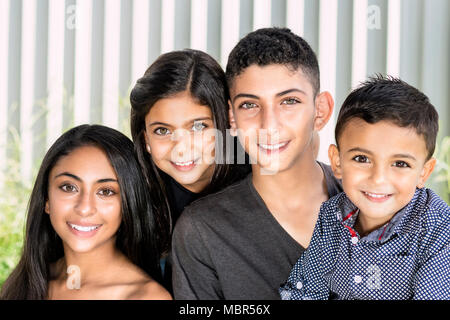 Lächelnd Geschwistern im Garten. Outdoor Portrait von zwei Brüder und zwei Schwestern, verschwommenes weiß Zaun Hintergrund. Stockfoto