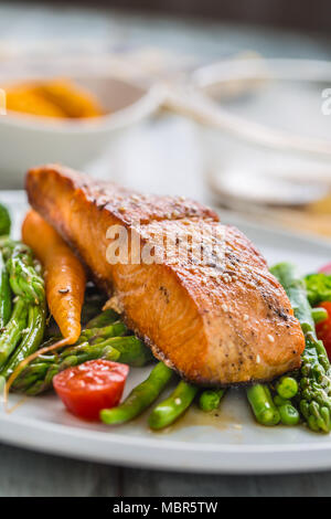 Gebratenes Lachssteak mit asparagos Brokkoli Möhren Tomaten Rettich grüne Bohnen und Erbsen. Fisch Mahlzeit mit frischem Gemüse. Stockfoto