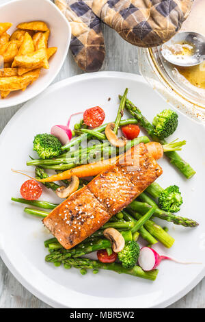 Gebratenes Lachssteak mit asparagos Brokkoli Möhren Tomaten Rettich grüne Bohnen und Erbsen. Fisch Mahlzeit mit frischem Gemüse. Stockfoto