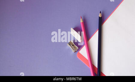 Bunte, fröhliche, bunte Bleistifte sind unten in einem Winkel und einem Notebook für Ihren Text auf einem violetten Hintergrund entfernt. Stockfoto