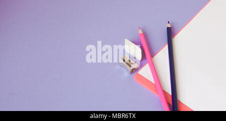 Bunte, fröhliche, bunte Bleistifte sind unten in einem Winkel und einem Notebook für Ihren Text auf einem violetten Hintergrund entfernt. Stockfoto