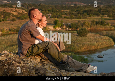 Junges Paar sitzt auf Felsen in der Nähe des Sees. Stockfoto