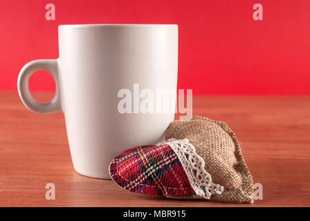 Tasse Kaffee und Herd auf hölzernen Schreibtisch und roten Hintergrund. Valentinstag Konzept Stockfoto