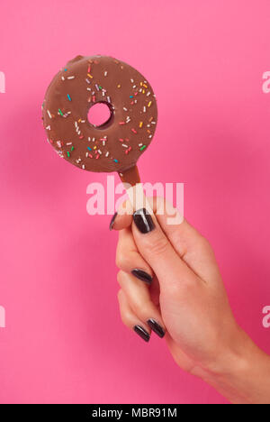 Donut Eis auf einem Stick holding Frauen Hand auf rosa Hintergrund Stockfoto