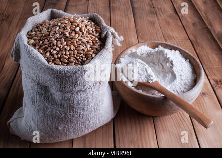 Weizen in Sack und vier in hölzerne Schüssel mit Löffel am Tisch Stockfoto