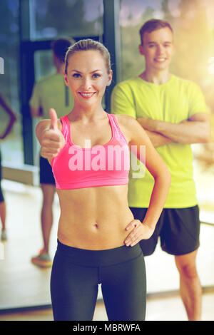 lächelnde Mann und Frau zeigt Daumen oben im Fitness-Studio Stockfoto