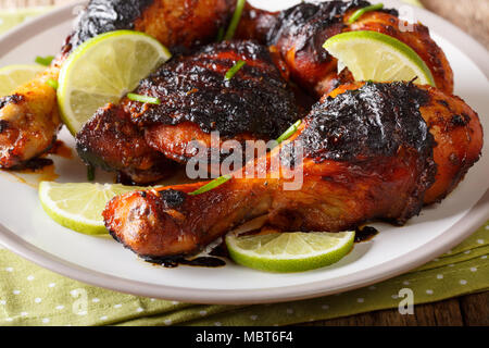 Die jamaikanische Essen: jerk chicken Drumstick mit Kalk closeup auf einem Teller auf den Tisch. Horizontale Stockfoto