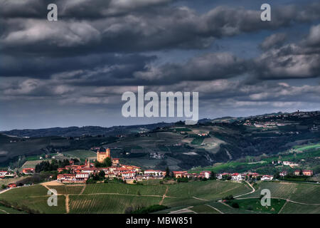 Weiten Blick über die Hügel und Weinberge der Langhe, unter einem stürmischen Himmel, während ein Sonnenstrahl erhellt Serralunga d'Alba und seine hoch aufragende Burg. Stockfoto