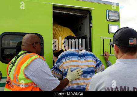 Mitglieder des Miami-Dade Feuerwehr Feuerwehr- und Rettungskräfte, unterstützen Freiwillige mit simulierten verletzt auf einem Rettungswagen bei einer gemeinsamen Übung von der Dade Feuerwehr und Homestead-Miami Speedway in Miami, Fla., Jan. 11, 2018 gehostet wird. Diese jte konzentrierte sich auf den Aufbau von Kapazitäten und der nahtlose Übergang zwischen den örtlichen Ersthelfern und die Unterstützung durch die Nationalgarde und aktiven Soldaten zur Verfügung gestellt. (U. S. Armee Foto von SPC. Samuel Brooks) Stockfoto