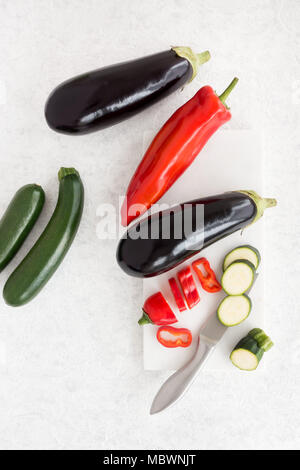 Blick von oben auf die Auberginen, Paprika und Zucchini auf weißem Marmor Schneidebrett hingewiesen. Stockfoto