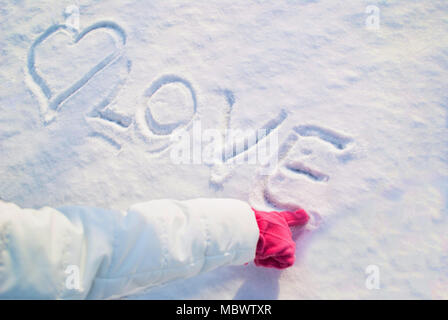 Finger in roten Handschuhe zeichnet ein Herz in den Schnee und das Wort Liebe Stockfoto