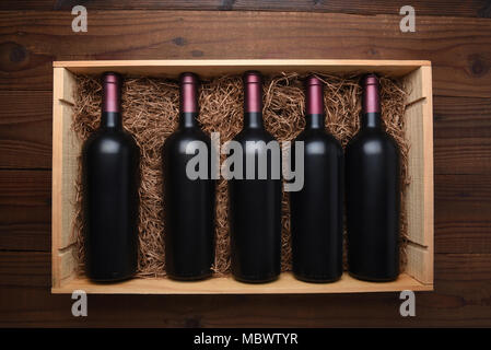 Bei Rotwein: Blick von oben auf ein Holz bei Rotwein Flaschen auf einem dunklen Holztisch, der Fall ist mit der Packung Stroh gefüllt. Stockfoto