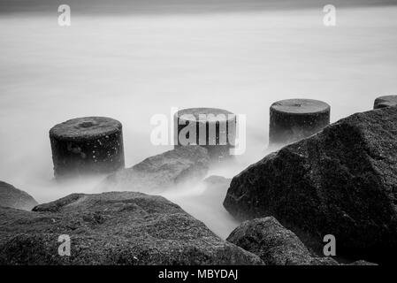 Pylone und Felsen Meer Wand mit konkreten defensive Blöcke und Wellen Stockfoto