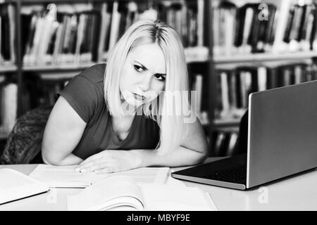 Weibliche Studenten sieht veraltet während des Studiums mit einem Laptop und Lehrbücher in der Bibliothek Stockfoto