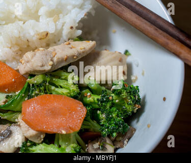 Huhn unter Rühren braten, in weiße Schüssel mit Reis, Essstäbchen, Abendessen winkel Aussicht serviert - chinesisches Essen Konzept Stockfoto