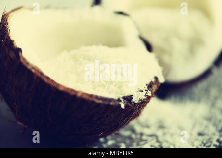 Coconut fuit Hälften mit Kokos Späne auf grauem Beton Hintergrund. Copyspace Stockfoto