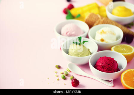 Eis Kugeln in Schalen, Waffeln, Beeren, Orange, Mango, Zitrone, Minze, Pistazien auf Rosa shabby chic Hintergrund. Bunte Sammlung, Sommer Konzept Stockfoto