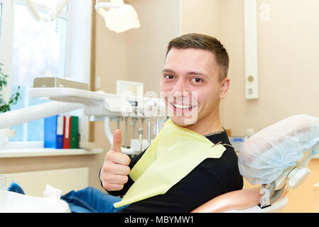 Glückliche junge Mann mit einem Lächeln sitzt in den zahnmedizinischen Stuhl Stockfoto