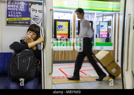 Tokio, Japan. Typische Szene an der Tokioter U-Bahn, mit einem sitzen junge Mädchen an Ihrem Mobiltelefon suchen, eine Anzeige und eine Lieferung Mann in Eile Stockfoto